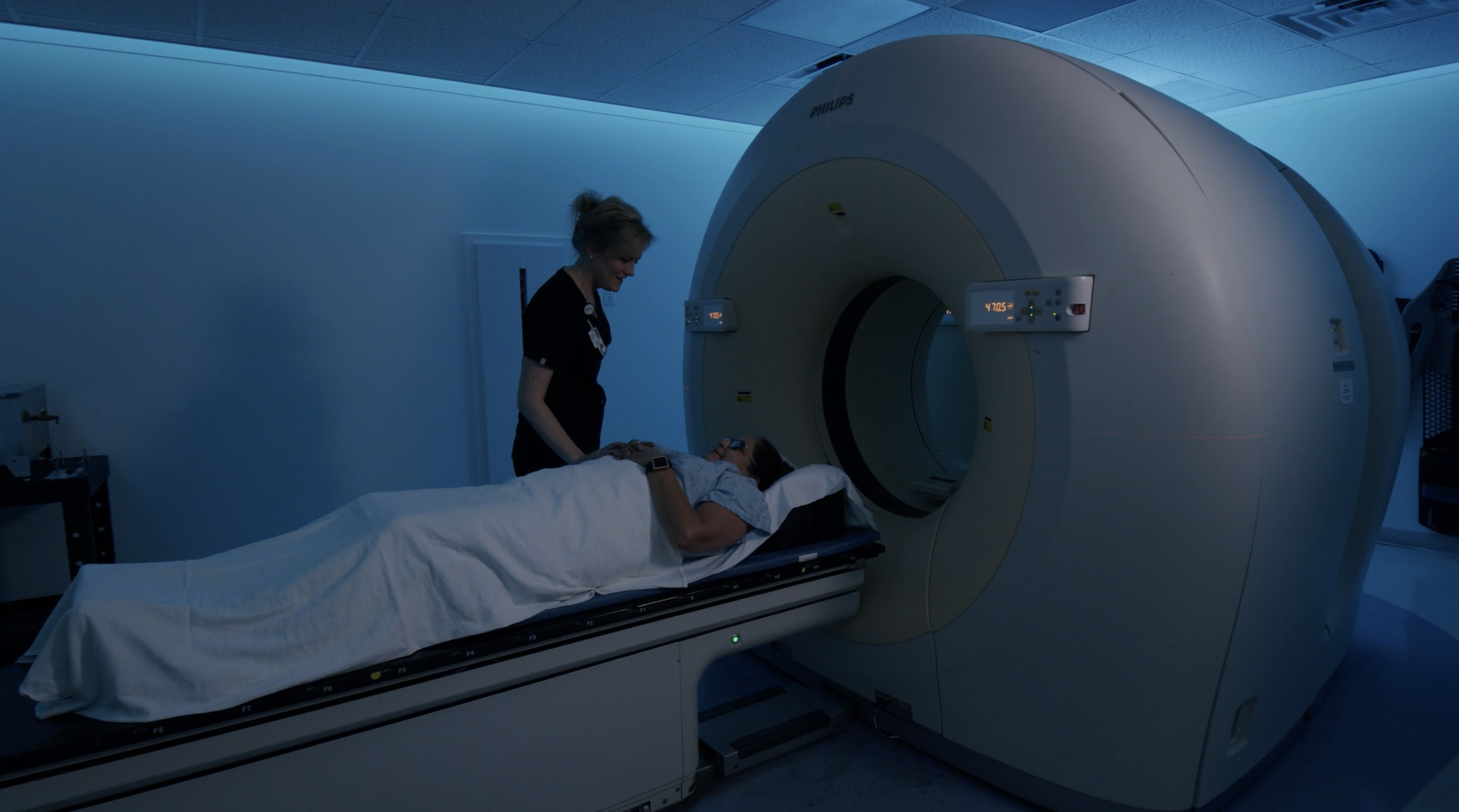 Patient on an imaging table beside a scanner with a healthcare professional