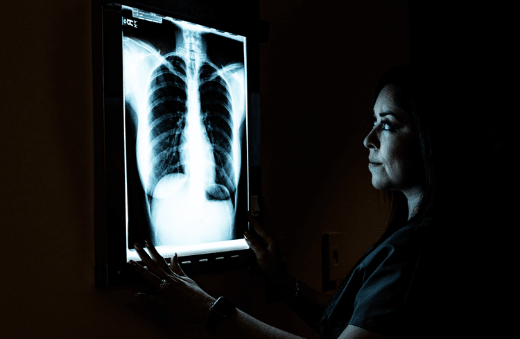 A woman examining a chest X-ray in a dark room.