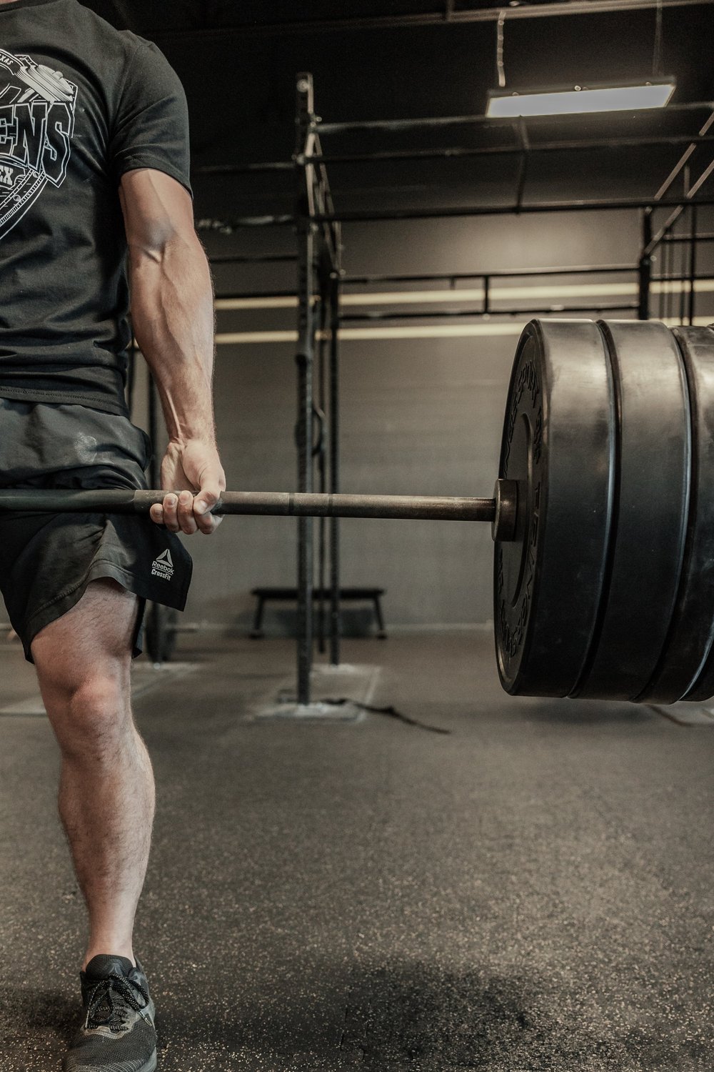 A person performing a deadlift exercise in a gym, holding a barbell loaded with large weight plates
